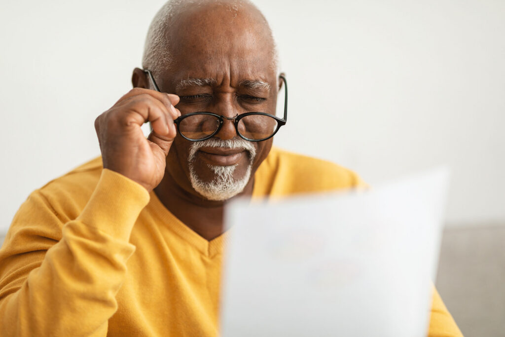 Older man with gray hair and beard wearing a yellow sweater, looking at a laptop.